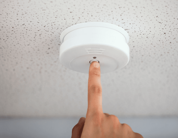 A hand pushing the test button of a smoke alarm.