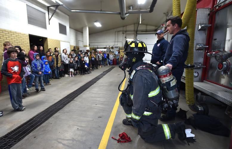 A group of childen learn about the gear a firefighter wears during a station tour.